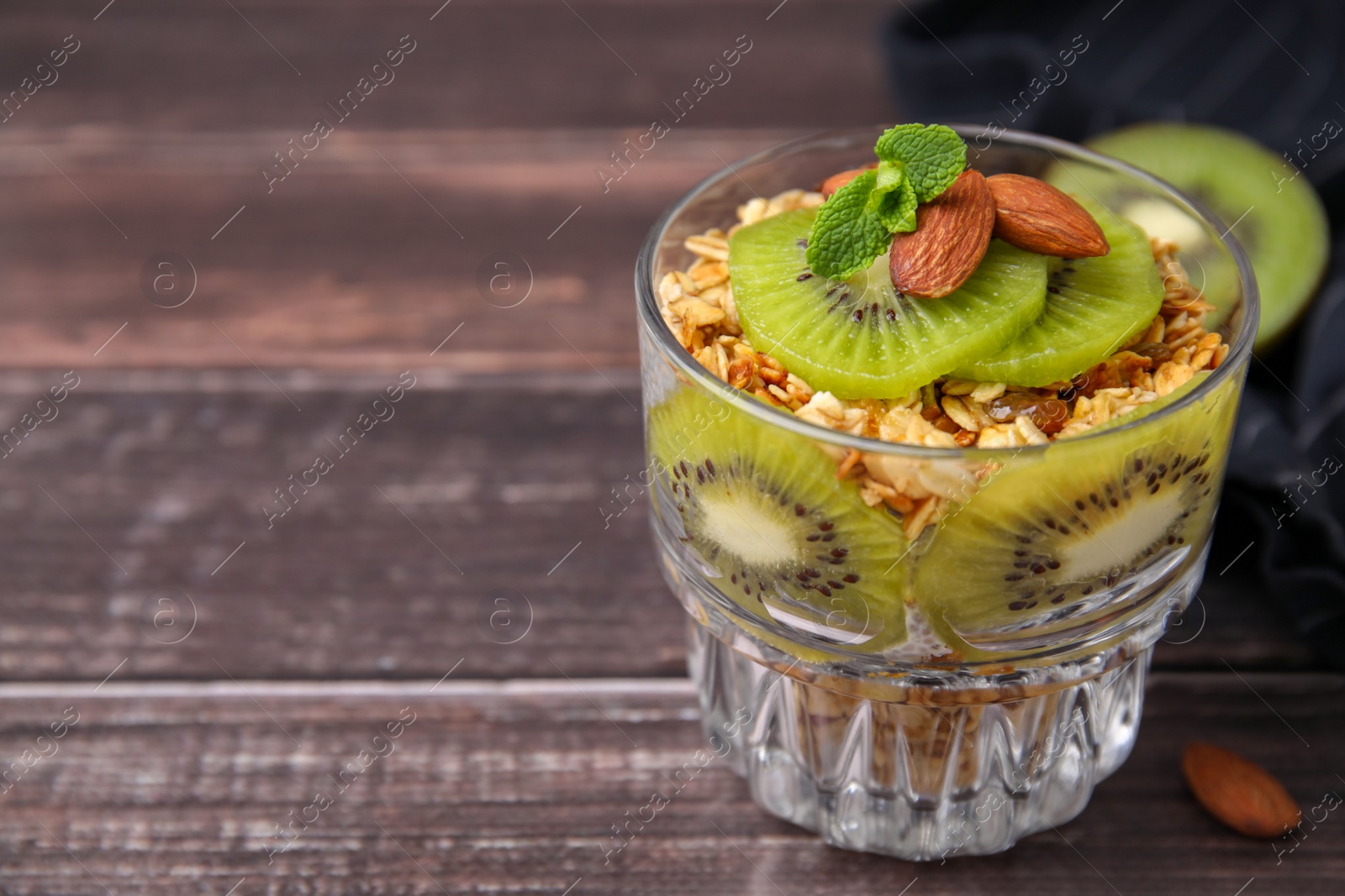 Photo of Delicious dessert with kiwi, muesli and almonds on wooden table, closeup. Space for text