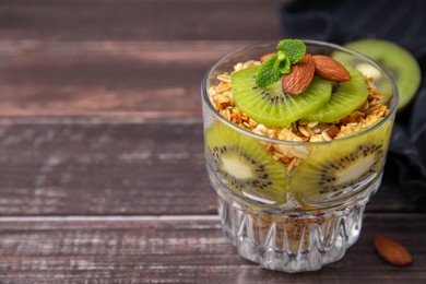 Delicious dessert with kiwi, muesli and almonds on wooden table, closeup. Space for text