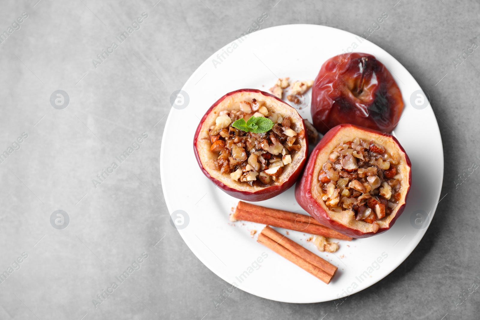 Photo of Tasty baked apples with nuts, honey, cinnamon sticks and mint on gray table, top view. Space for text