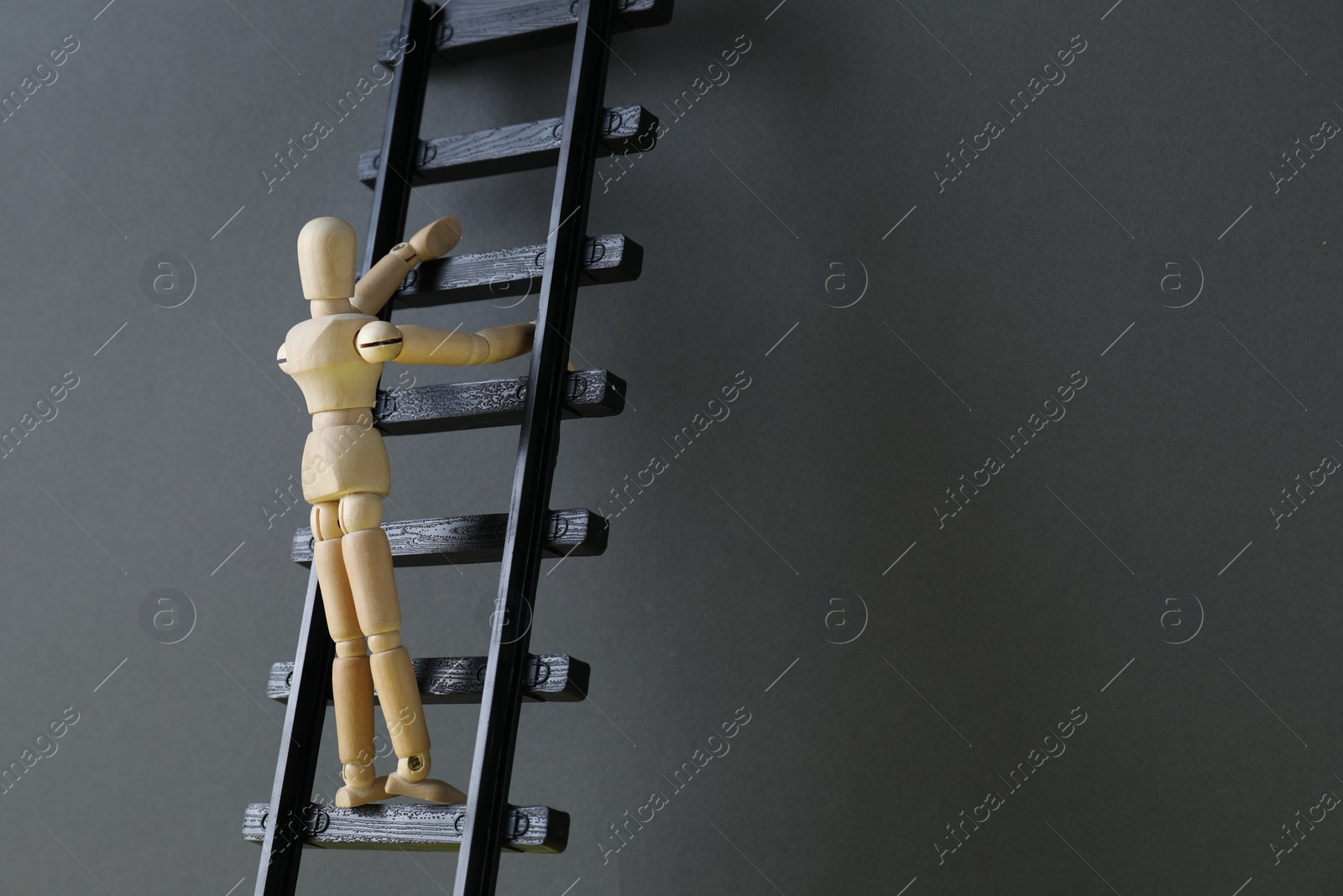Photo of Overcoming barries for development and success. Wooden human figure climbing up toy ladder near grey wall, space for text