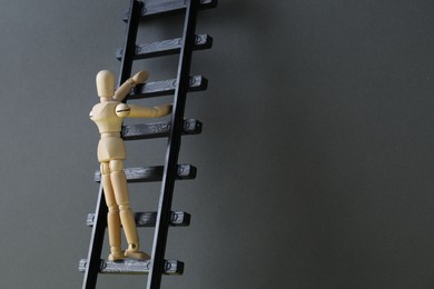 Overcoming barries for development and success. Wooden human figure climbing up toy ladder near grey wall, space for text