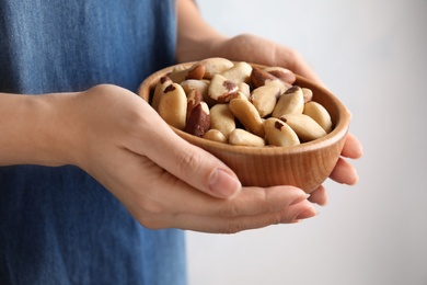Photo of Woman holding bowl with Brazil nuts on grey background, closeup