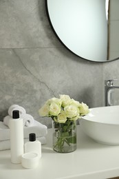 Photo of Beautiful roses and bath accessories near sink in bathroom