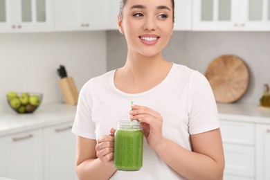 Beautiful young woman holding mason jar with delicious smoothie in kitchen