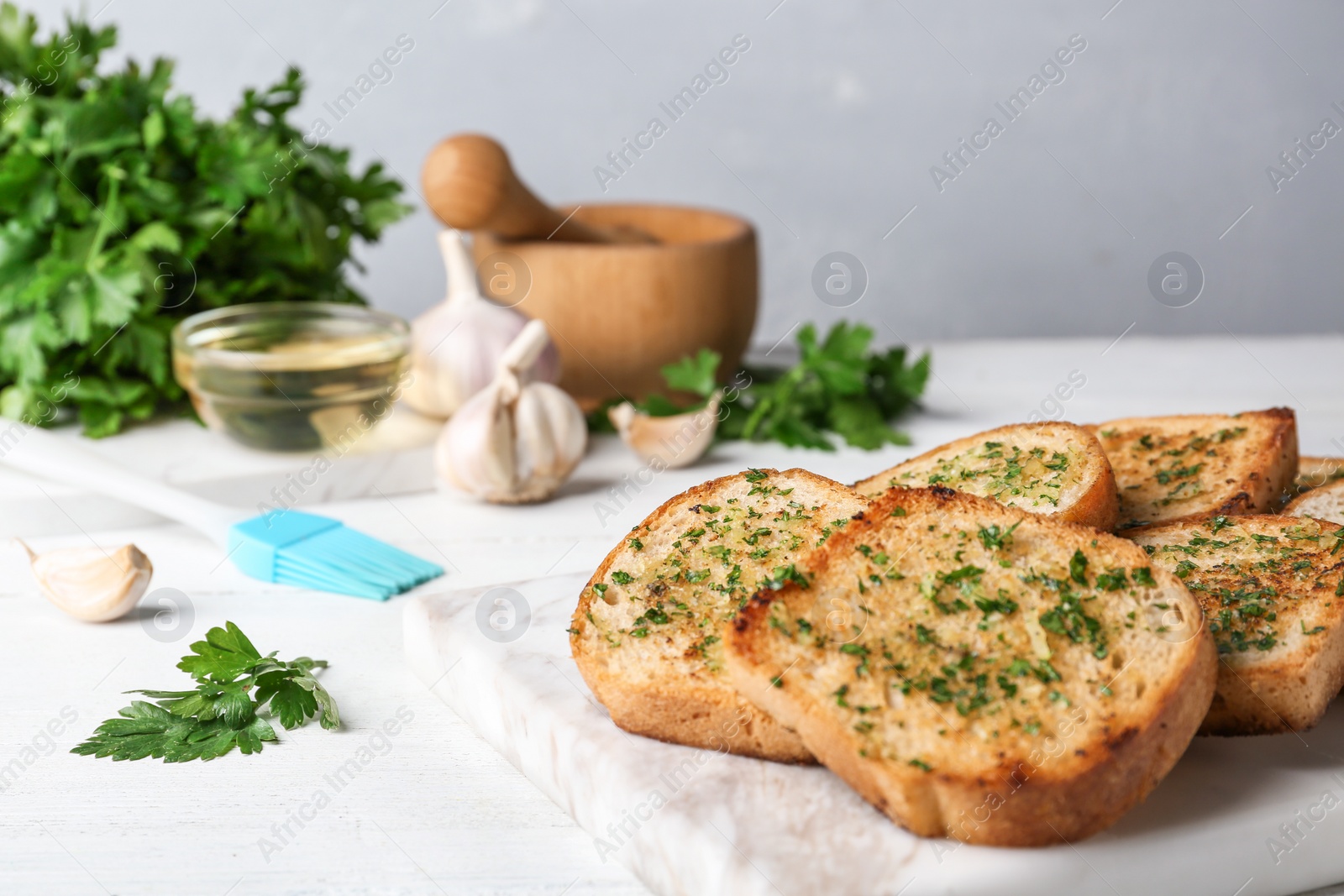 Photo of Slices of toasted bread with garlic and herbs on white wooden table