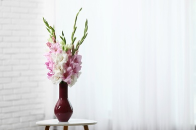 Photo of Vase with beautiful gladiolus flowers on wooden table indoors. Space for text