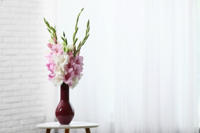 Vase with beautiful gladiolus flowers on wooden table indoors. Space for text