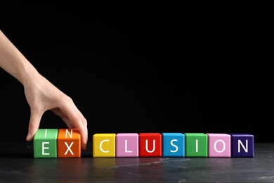 Photo of Woman making word Inclusion with colorful cubes on marble table against black background, closeup. Space for text