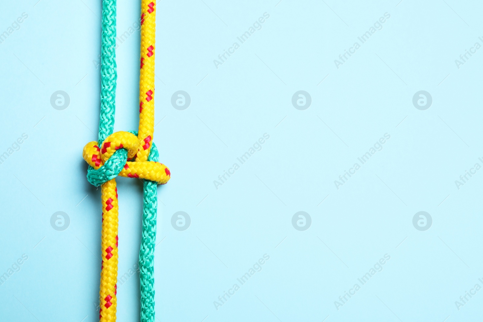 Photo of Top view of colorful ropes tied with knot on light blue background, space for text. Unity concept