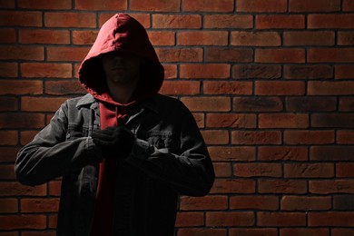 Photo of Thief in hoodie against red brick wall. Space for text