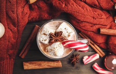 Flat lay composition with glass cup of tasty cocoa and Christmas candy cane on wooden table