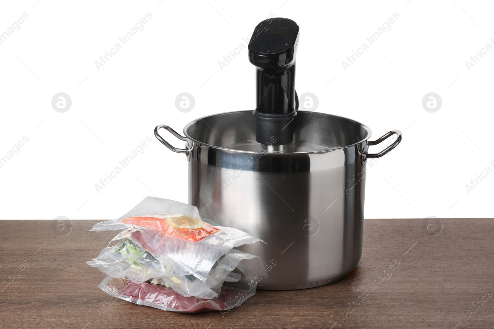 Photo of Sous vide cooker in pot and vacuum packed food products on wooden table against white background. Thermal immersion circulator