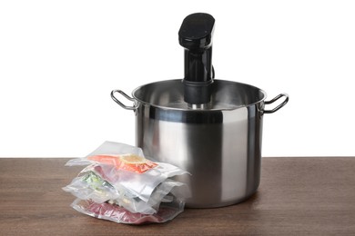 Photo of Sous vide cooker in pot and vacuum packed food products on wooden table against white background. Thermal immersion circulator