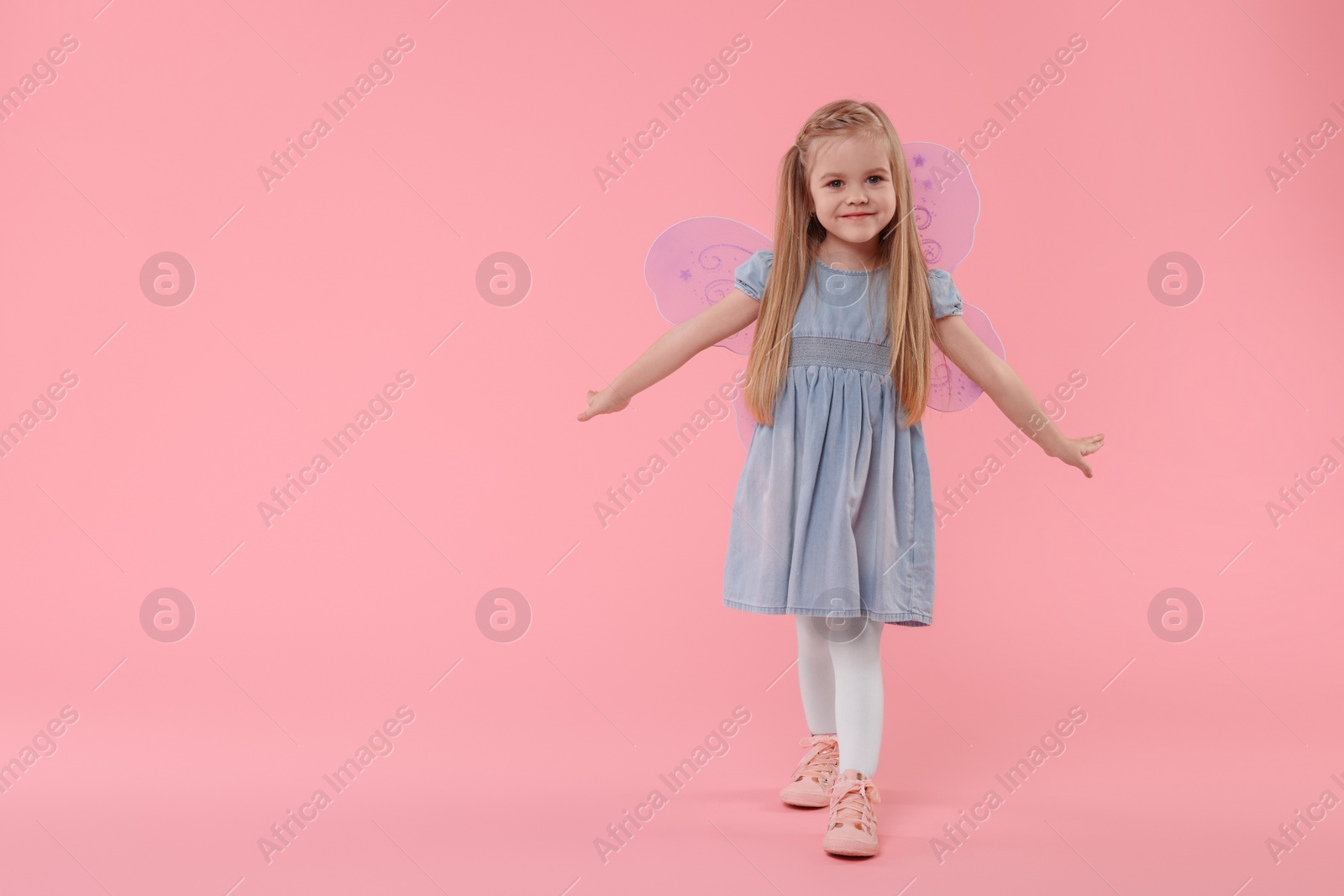 Photo of Cute little girl in fairy costume with violet wings on pink background, space for text