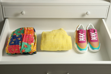 Photo of Sneakers and folded clothes in open drawer. Apparel storage