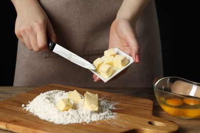 Photo of Woman adding fresh butter onto board with flour at wooden table, closeup