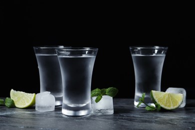 Photo of Shot glasses of vodka with lime slices, ice and mint on grey table