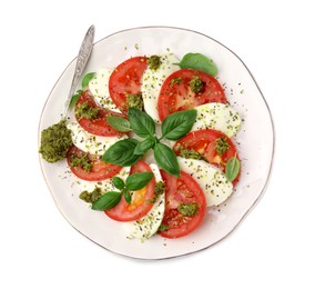 Photo of Plate of delicious Caprese salad and spoon with pesto sauce isolated on white, top view