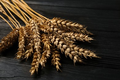 Photo of Bunch of wheat on black wooden table, closeup