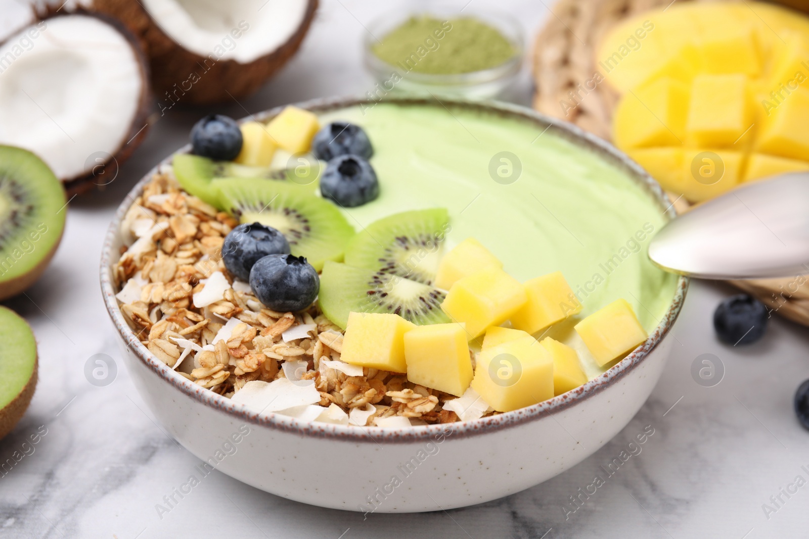 Photo of Tasty matcha smoothie bowl with fresh fruits and oatmeal served on white marble table, closeup. Healthy breakfast