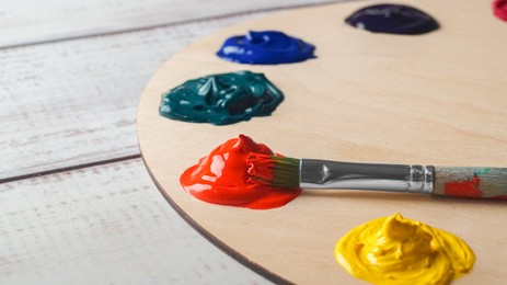 Photo of Artist's palette with samples of colorful paints and brush on white wooden table, closeup. Space for text