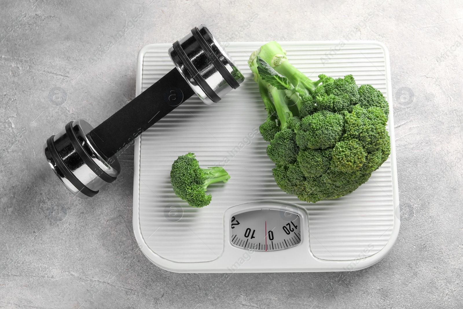 Photo of Healthy diet. Scale, broccoli and dumbbell on grey table, top view