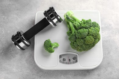 Photo of Healthy diet. Scale, broccoli and dumbbell on grey table, top view