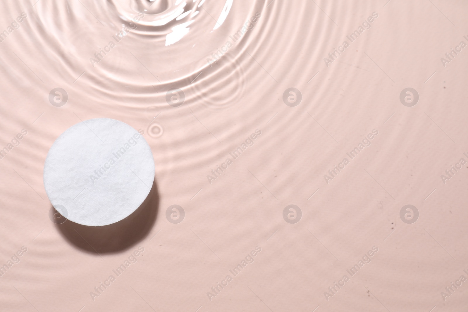 Photo of Cotton pad in micellar water on beige background, top view. Space for text