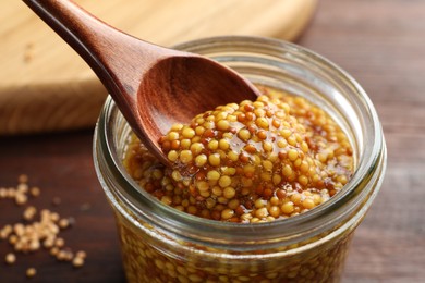 Taking whole grain mustard with spoon from jar on table, closeup