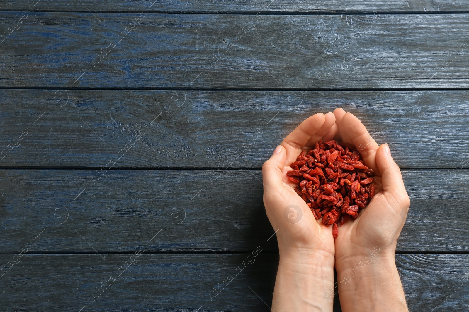 Photo of Woman holding red dried goji berries on blue wooden background, top view. Space for text