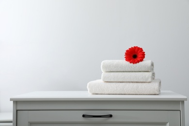 Photo of Stack of fresh towels with flower on cabinet against white background. Space for text