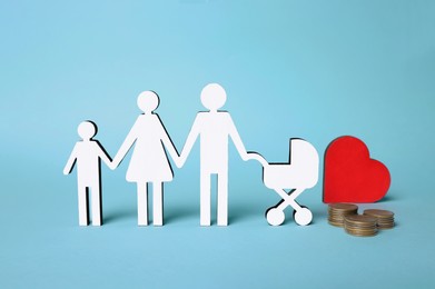 Photo of Figures of family stainding near heart and coins on light blue background. Insurance concept