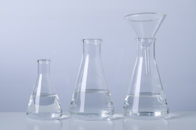Photo of Conical flasks with transparent liquid and funnel on table against light background