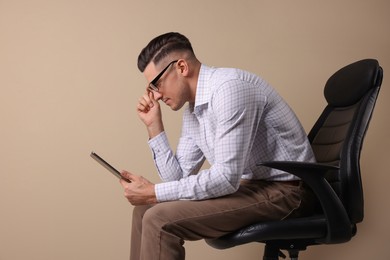 Photo of Man with poor posture using tablet while sitting on chair against beige background