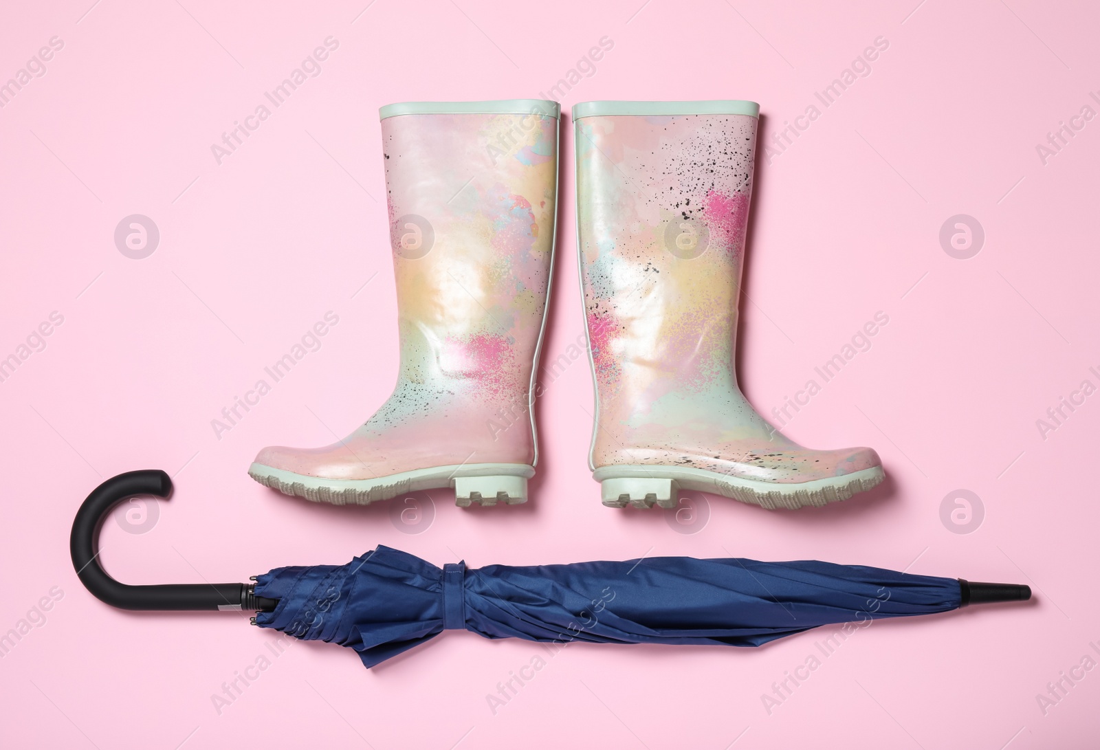 Photo of Pair of rubber boots near blue umbrella on pink background, flat lay