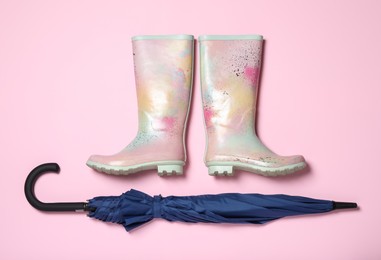 Pair of rubber boots near blue umbrella on pink background, flat lay