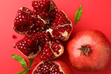 Photo of Fresh pomegranates and green leaves on red background, flat lay