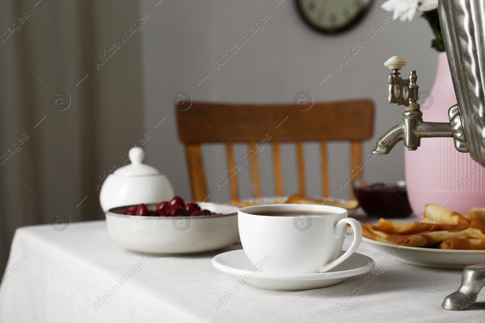 Photo of Vintage samovar, cup of hot drink and snacks served on table indoors. Traditional Russian tea ceremony