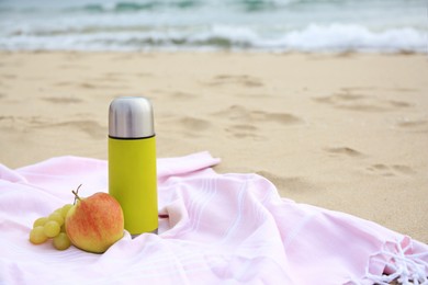 Metallic thermos with hot drink, fruits and plaid on sandy beach near sea, space for text