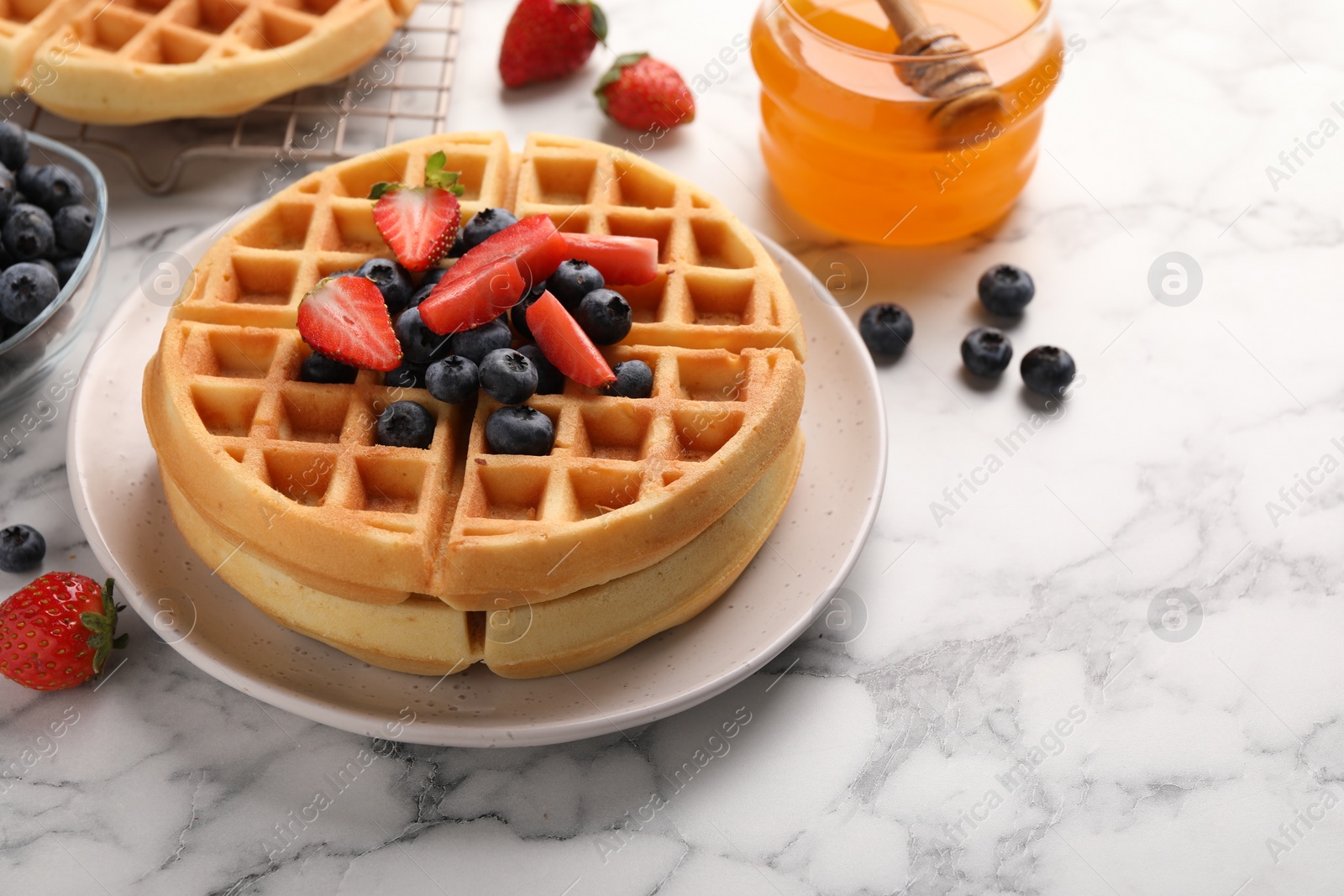 Photo of Tasty Belgian waffles with fresh berries and honey on white marble table, space for text