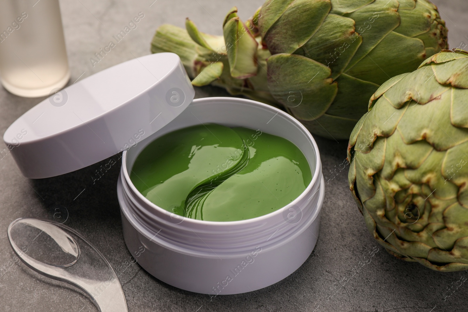 Photo of Package of under eye patches and artichokes on grey table, closeup. Cosmetic product