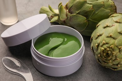 Photo of Package of under eye patches and artichokes on grey table, closeup. Cosmetic product