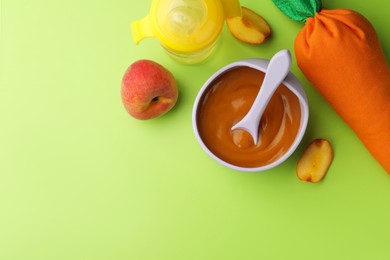 Photo of Healthy baby food in bowl and fresh peaches on light green background, flat lay. Space for text