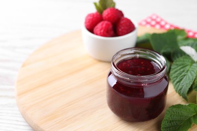 Jar of delicious raspberry jam, fresh berries and green leaves on wooden board, closeup. Space for text