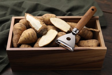Photo of Tubers of turnip rooted chervil and peeler in wooden crate on table, closeup