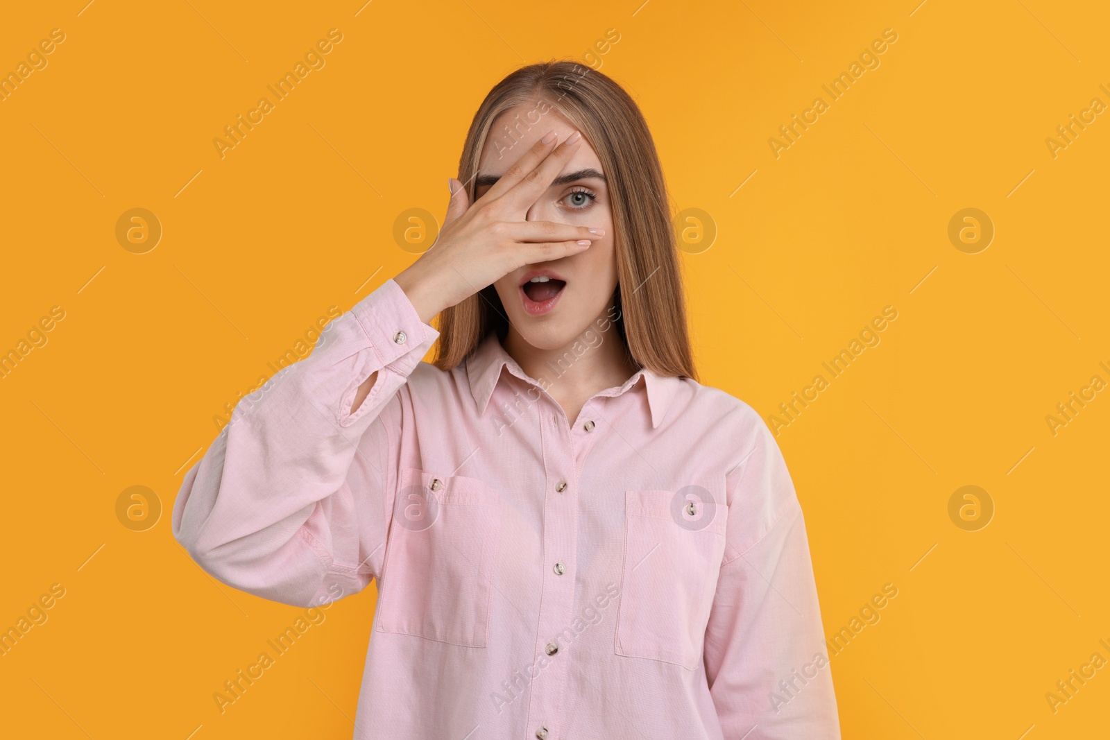 Photo of Embarrassed woman covering face with hand on orange background