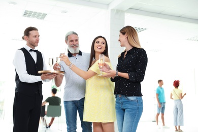 Photo of Waiter serving champagne to group of people at exhibition in art gallery