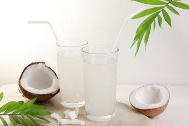 Glasses of coconut water, palm leaves and nuts on white table