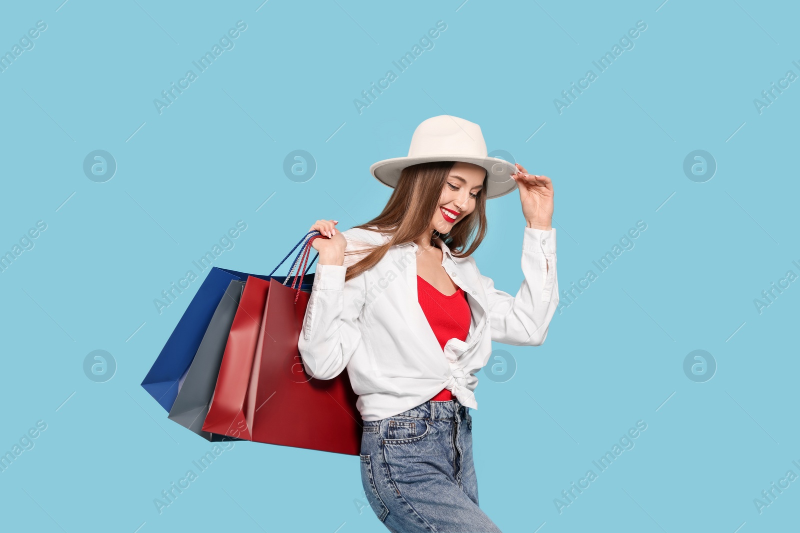 Photo of Stylish young woman with shopping bags on light blue background