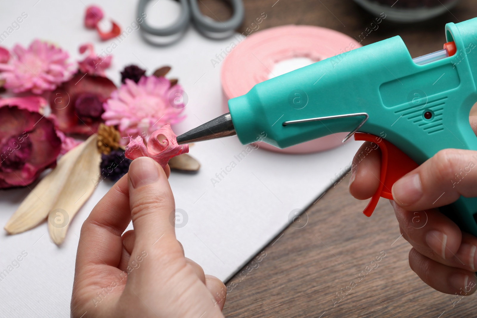 Photo of Woman using hot glue gun to make craft at wooden table, closeup